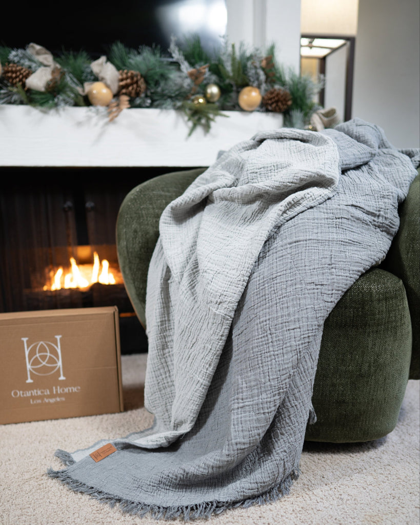 A sage muslin blanket cascading down from the chair to the floor in a warm, cozy holiday-themed living space.