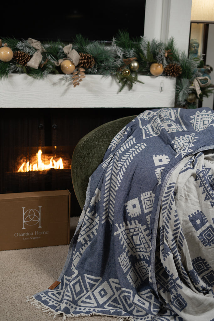 Close-up view of dark blue boho blanket draped over a chair beside a fireplace with Christmas decorations.