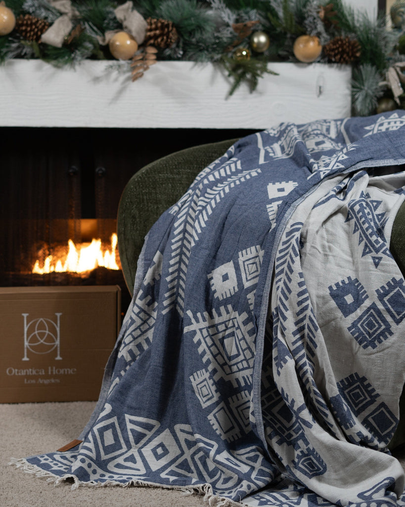 Dark blue and ivory boho blanket draped over a green chair by a fireplace, reversible geometric pattern visible.