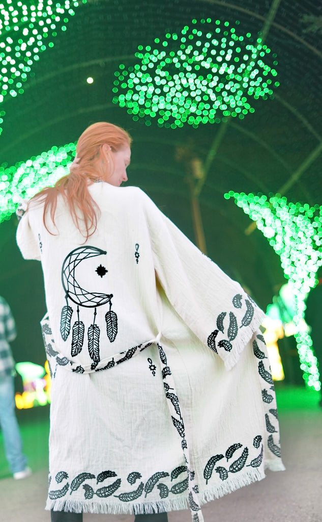 Dreamcatcher Kimono in motion as the model walks through illuminated festival lights, revealing the reversible dreamcatcher motif, flowing organic cotton drape, and airy unisex boho fit.