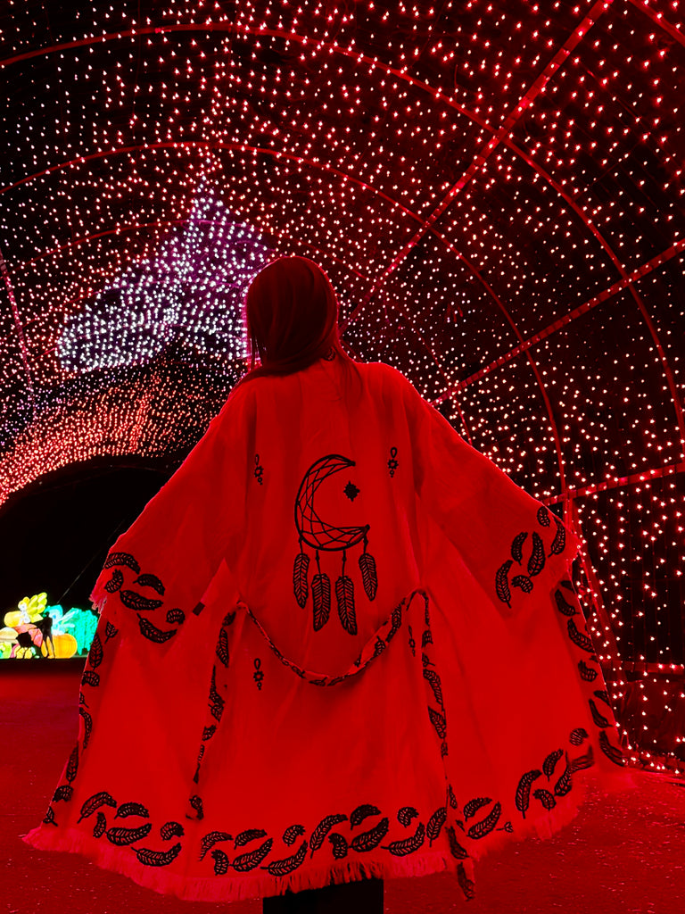 Dreamcatcher Kimono styled in a vibrant festival setting with red lights, showcasing the bold dreamcatcher back design, flowing unisex silhouette, bohemian aesthetic, and lightweight organic cotton movement.
