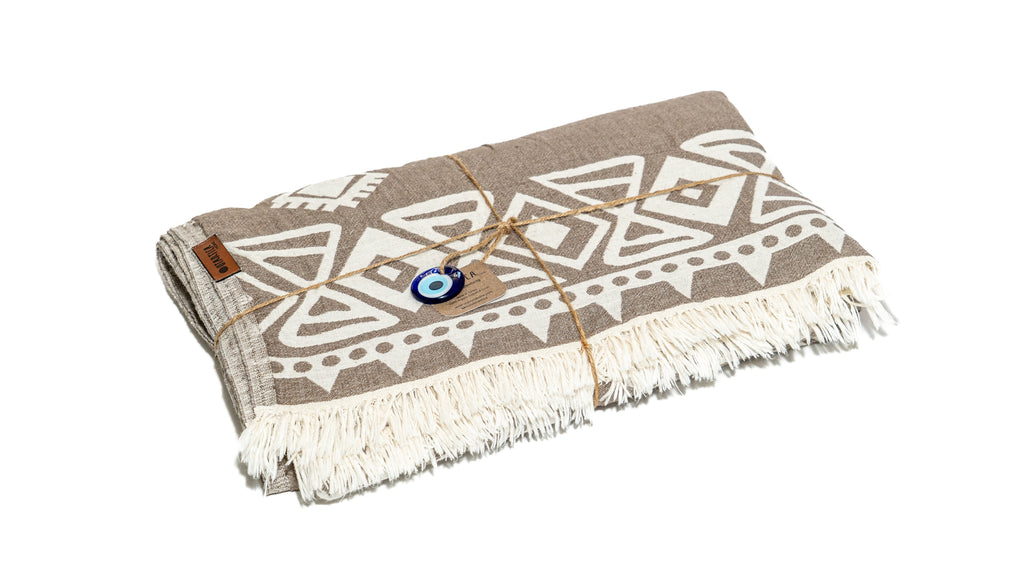 Folded sand boho blankets with evil eye charms next to an Otantica Home gift box, ready for gifting