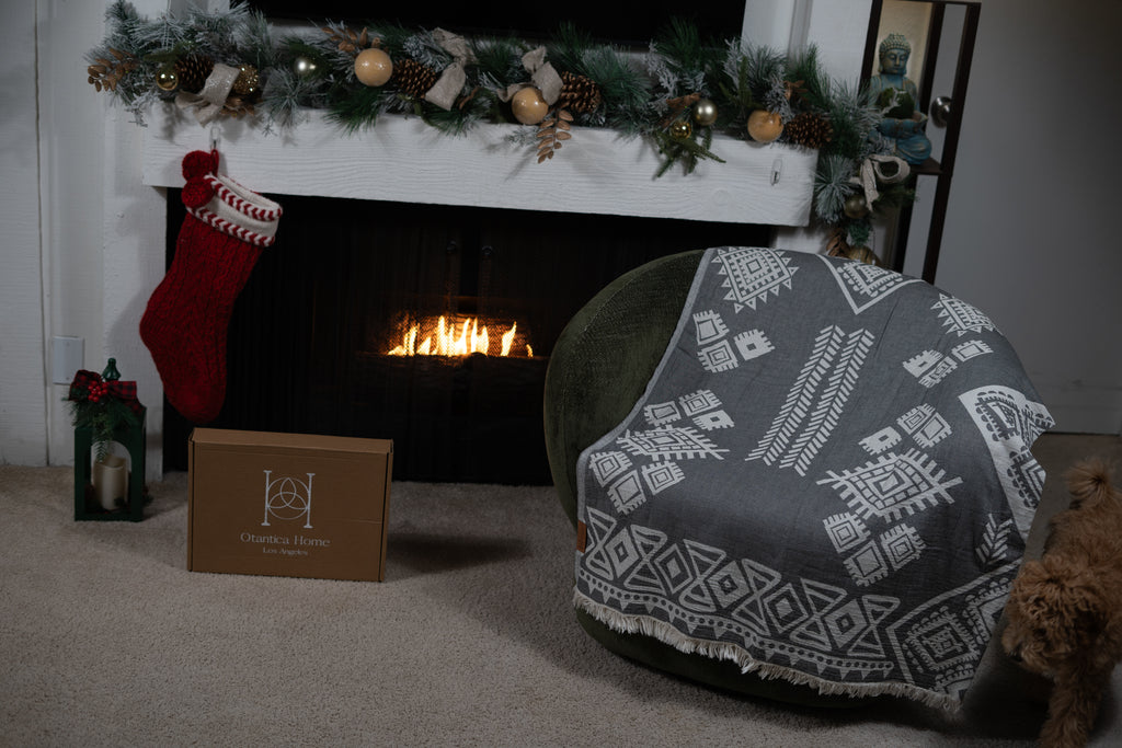 Grey boho throw blanket displayed over chair with Otantica Home gift box and Christmas decor.