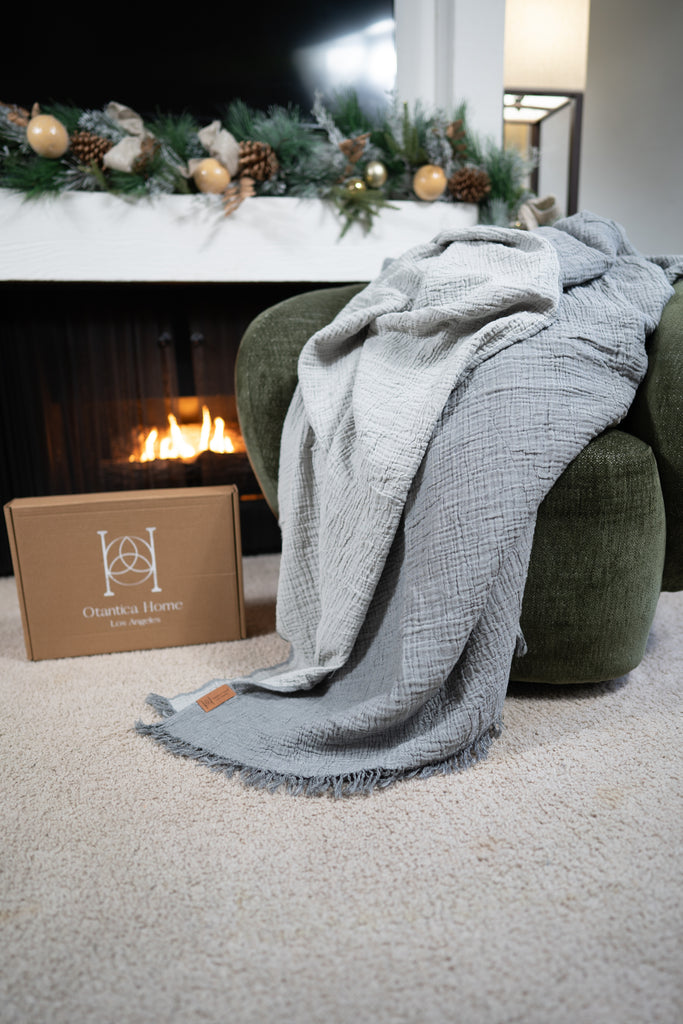 Grey muslin blanket displayed on a green chair in a holiday living room setting, highlighting soft airy gauze texture.