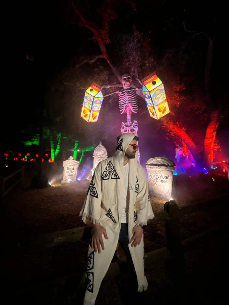 Night shot of the Veni Vidi Vici Kimono under vibrant festival lights, showcasing hooded design, geometric spiritual symbols and unisex bohemian style.