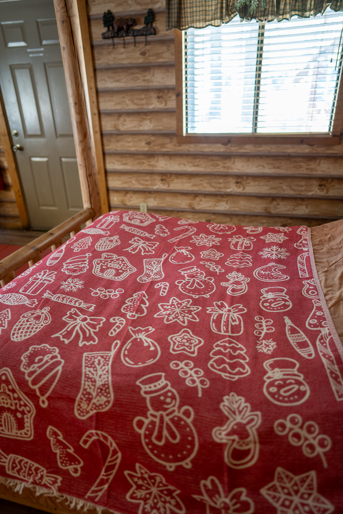 Red and white Christmas-themed organic cotton blanket spread on a wooden cabin bed.