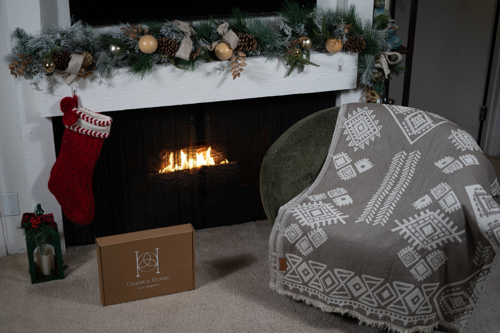 Set of boho organic cotton blankets in sand and neutral tones styled as a holiday gift set in front of a fireplace