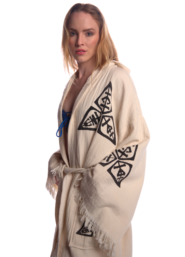 Side portrait of the Veni Vidi Vici Kimono on a female model, showcasing the detailed woven black geometric symbols on soft beige organic cotton fabric.