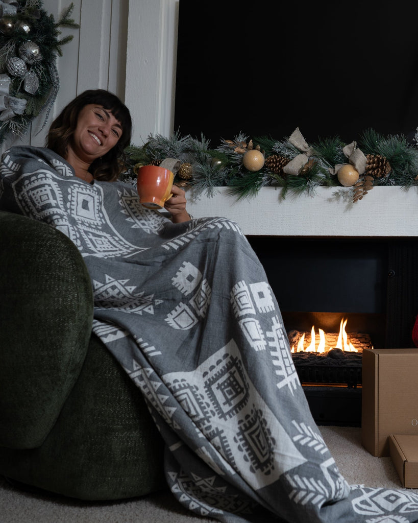 Woman relaxing with grey reversible boho blanket by Otantica Home in a holiday living room.