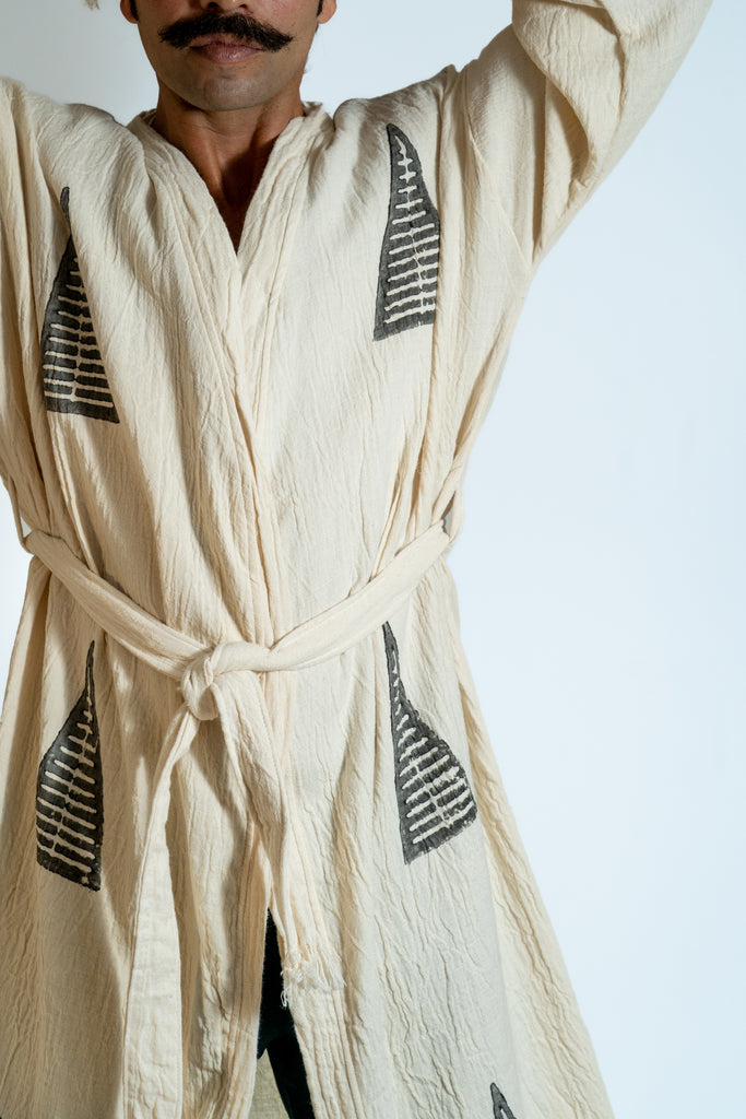 Man wearing beige tribal kimono with black ancient symbols, tied waist belt, minimal studio background