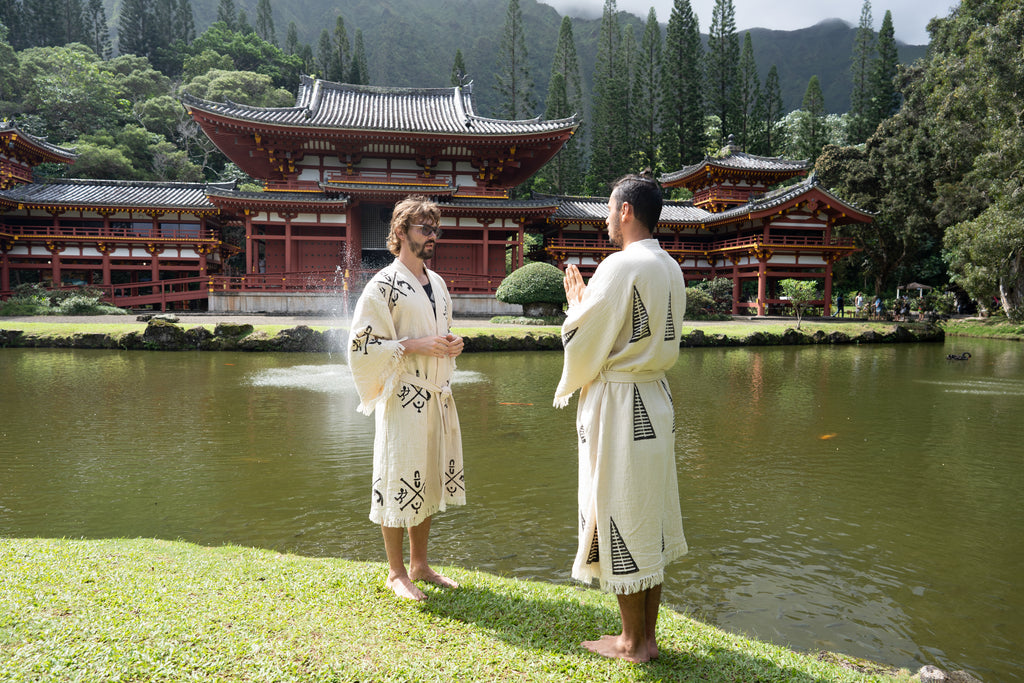 Two men wearing tribal embroidered kimonos near Japanese temple garden, natural outdoor setting