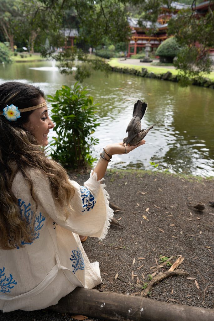 Woman sitting lakeside in Reef Kimono, blue coral motifs visible, surrounded by nature and temple scenery.