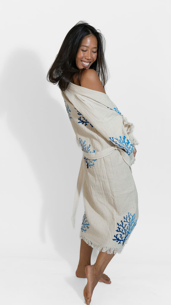 Woman wearing Organic Reef Kimono with blue coral embroidery, posing in a soft off-shoulder angle on white background.