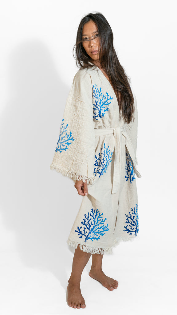 Woman wearing Reef Kimono with blue coral patterns, relaxed stance, photographed in a minimal white studio.