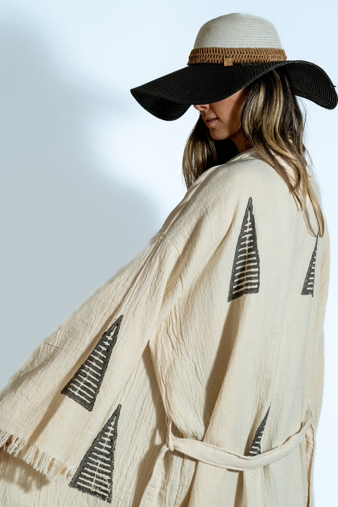 Woman wearing beige tribal kimono with black geometric symbols, wide sleeves, artistic side pose in studio